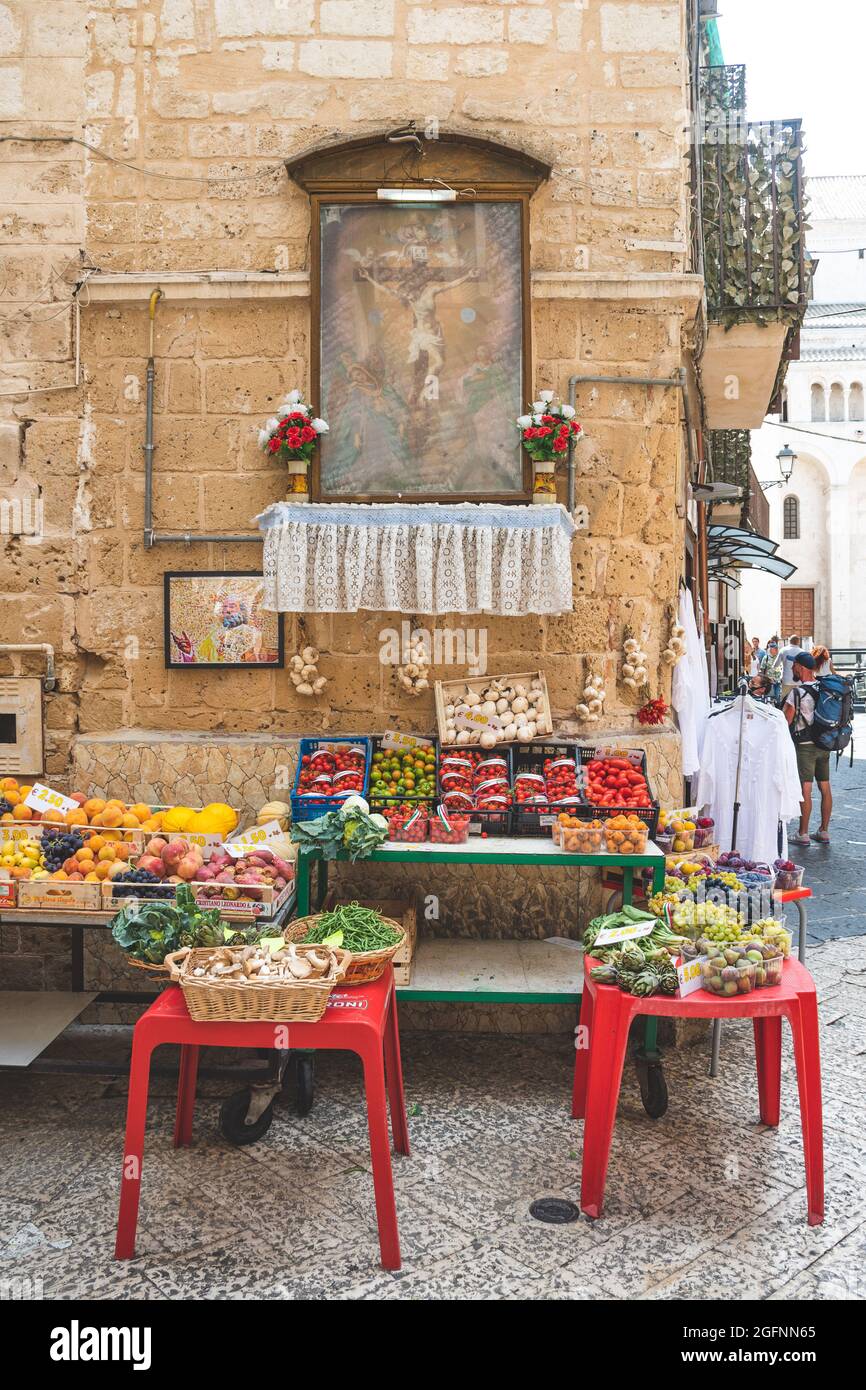 Vista su una stradina nel centro storico di Bari, Puglia, Italia, tradizionale negozio di frutta all'aperto con immagini religiose e vari tipi di frutta e verdura locali Foto Stock