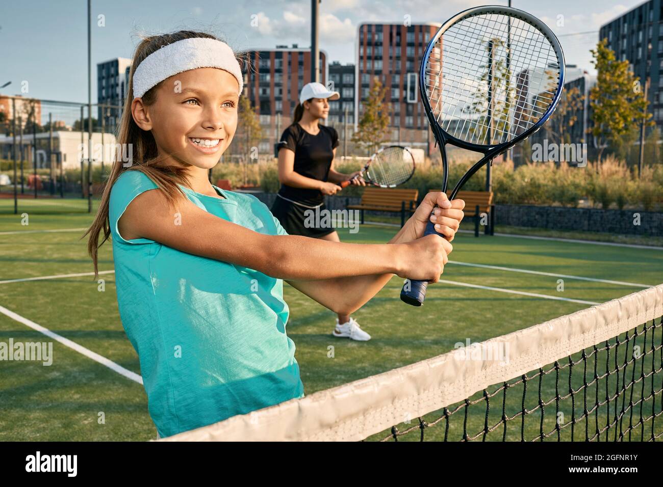 Piccola ragazza sorridente giocatore di tennis con il suo partner allenatore che gioca raddoppia a tennis sul campo d'erba in giorno di sole Foto Stock