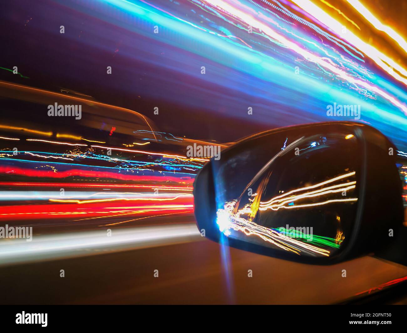 Corsie al neon blu, arancione e rosso illuminano a lungo l'esposizione durante la guida in auto ad alta velocità nella città notturna e il suo riflesso nello specchio retrovisore Foto Stock