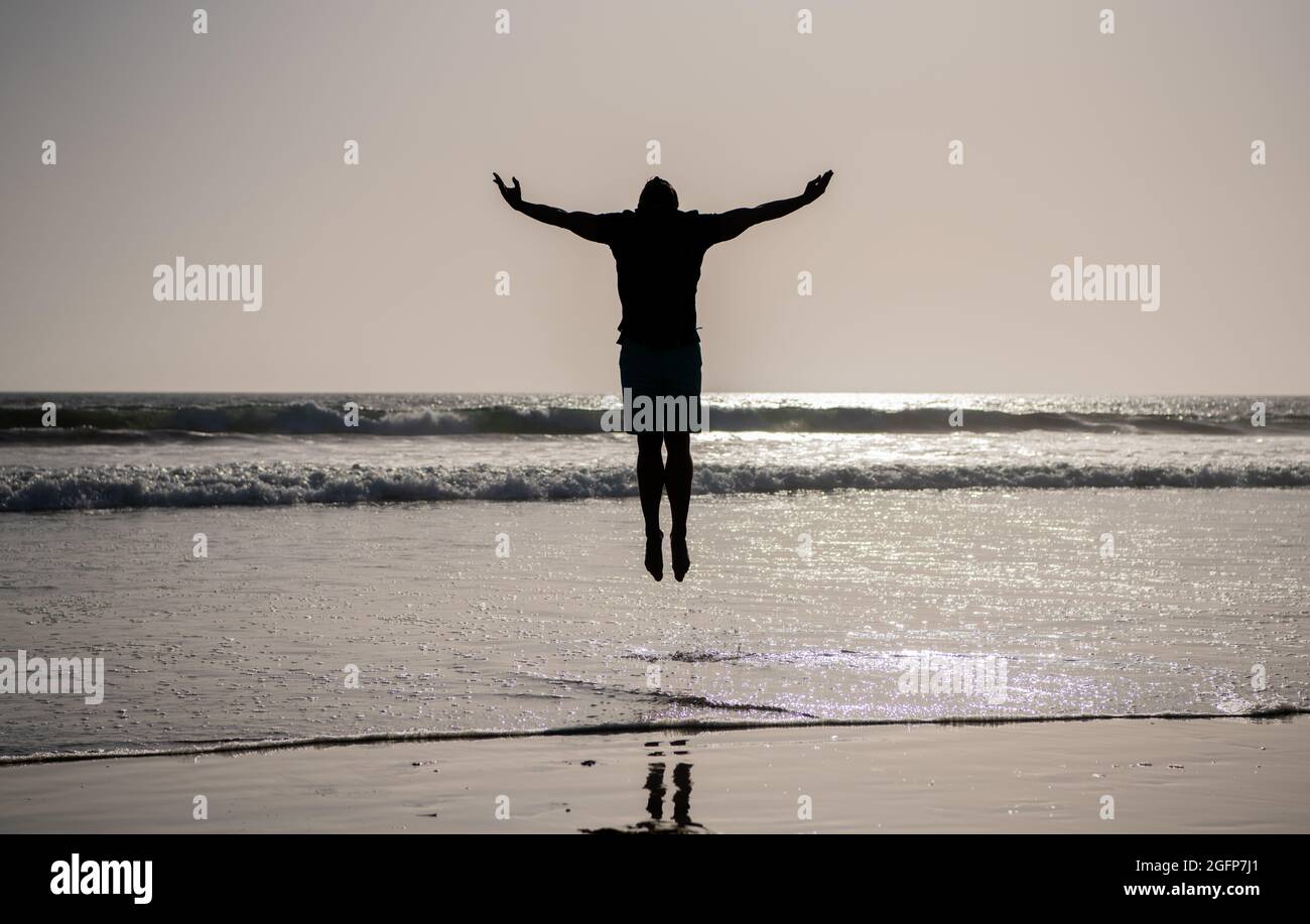 silhouette di uomo atletico salto con le mani rialzate sulla spiaggia estiva, ispirazione Foto Stock