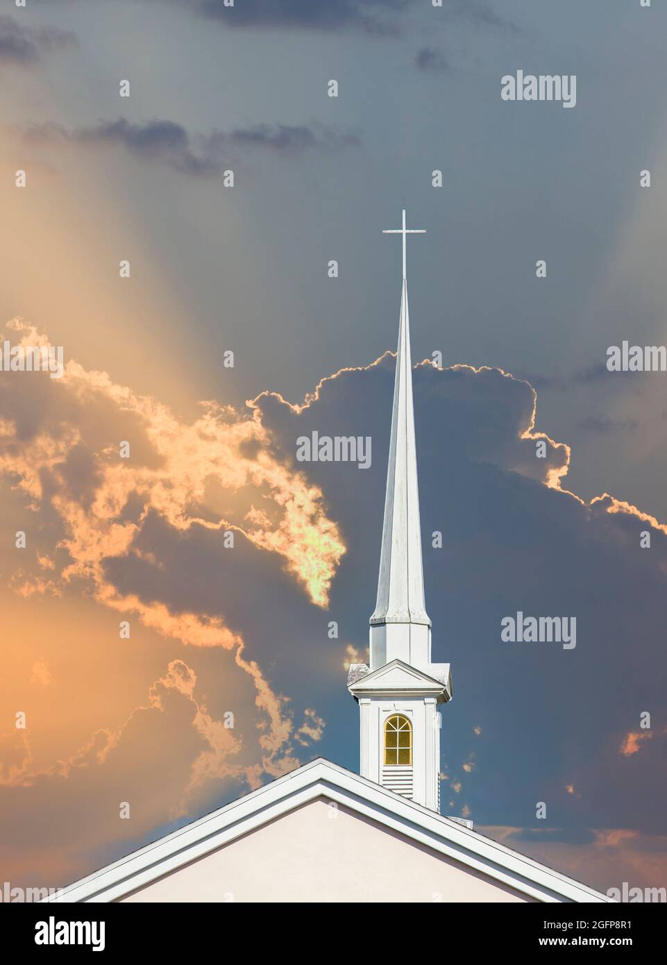 Alto campanile di chiesa bianca con croce sulla cima aganista un cielo arancione con raggi solari a Punta Gorda Florida Foto Stock