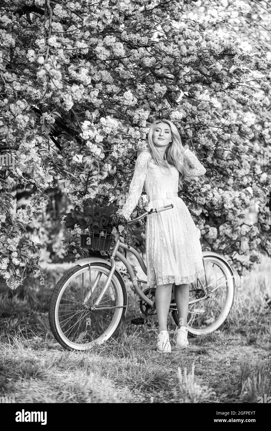 Stile primaverile. Fiore di ciliegio rosa. Ragazza porta fiori in bicicletta retrò. Primavera bella donna in abito. Ragazza con moto d'epoca. Fiore sakura Foto Stock