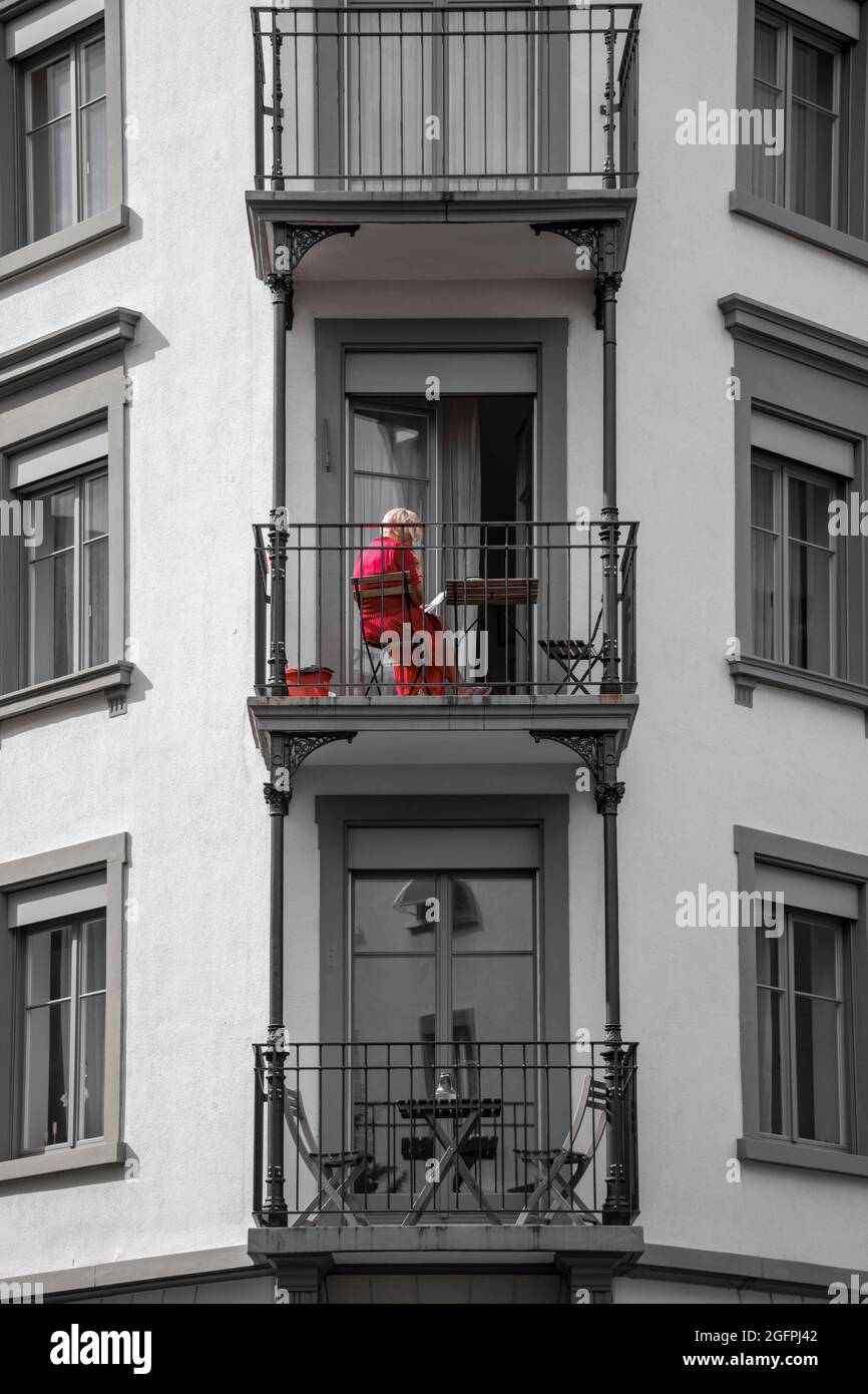 Signora in rosso seduto sul suo balcone e leggere un libro Foto Stock