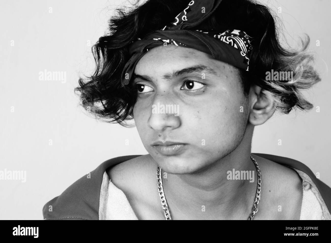 Scatto in scala di grigi di un ragazzo del sud asiatico serio dall'India con i capelli lunghi dell'ombre che portano una bandana Foto Stock