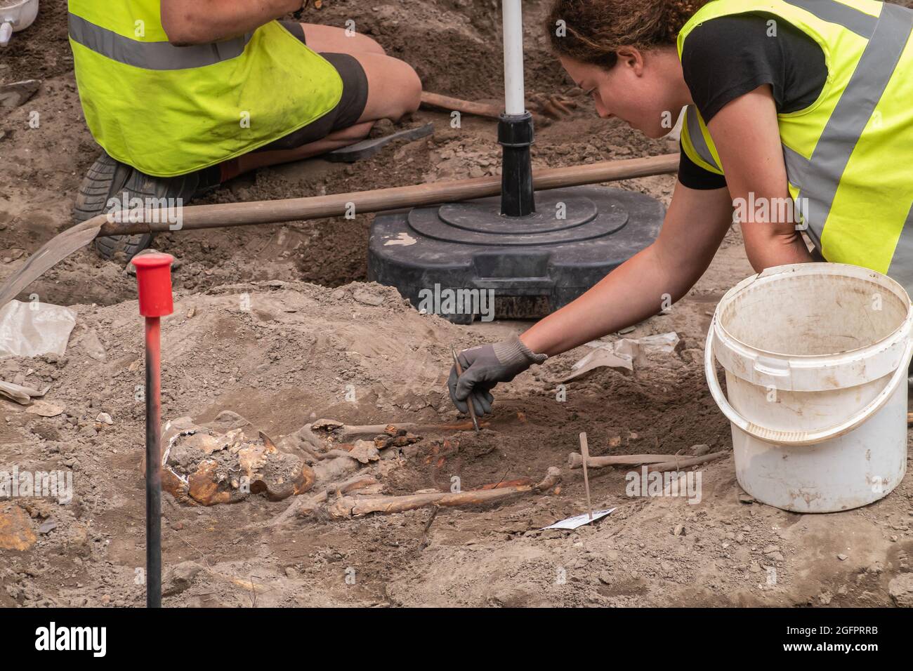Brugge, Fiandre, Belgio - 4 agosto 2021: La donna pulisce lo sporco dallo scheletro vicino allo scavo archeologico sull'ex cimitero appena fuori Onze lieve Vro Foto Stock