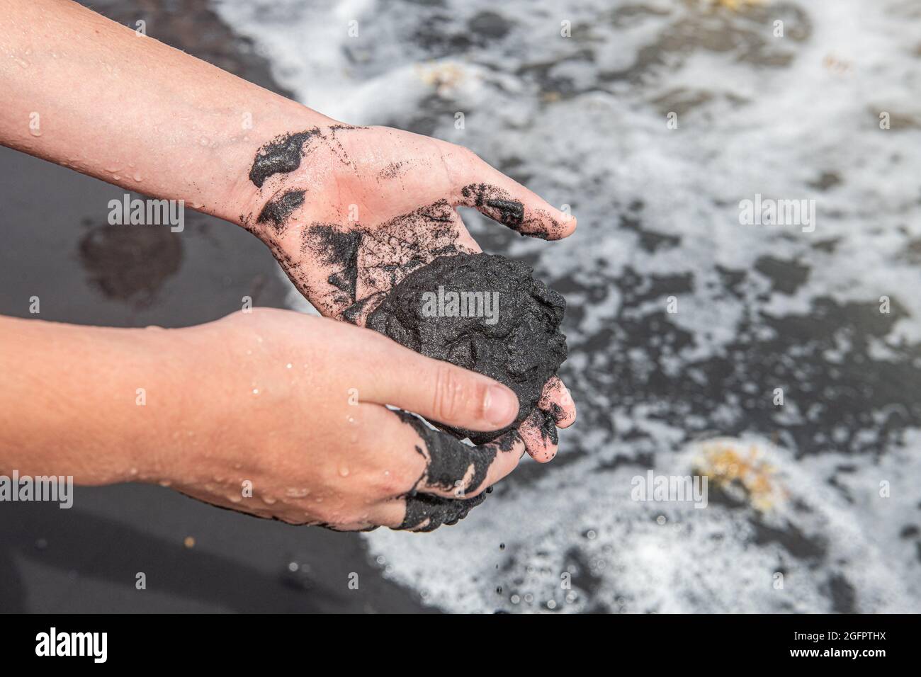 Mani che tengono un grumo di sabbia nera bagnata - Porto Rico Foto Stock