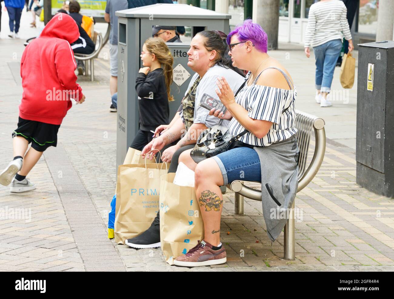 Donna con capelli viola, e tatuaggio sulla gamba, riposante dopo lo shopping Foto Stock