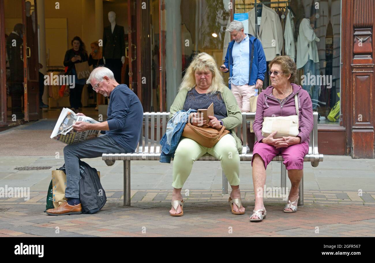 Ci sono persone sedute su una panchina, ognuna si è avvincita a modo loro. Foto Stock