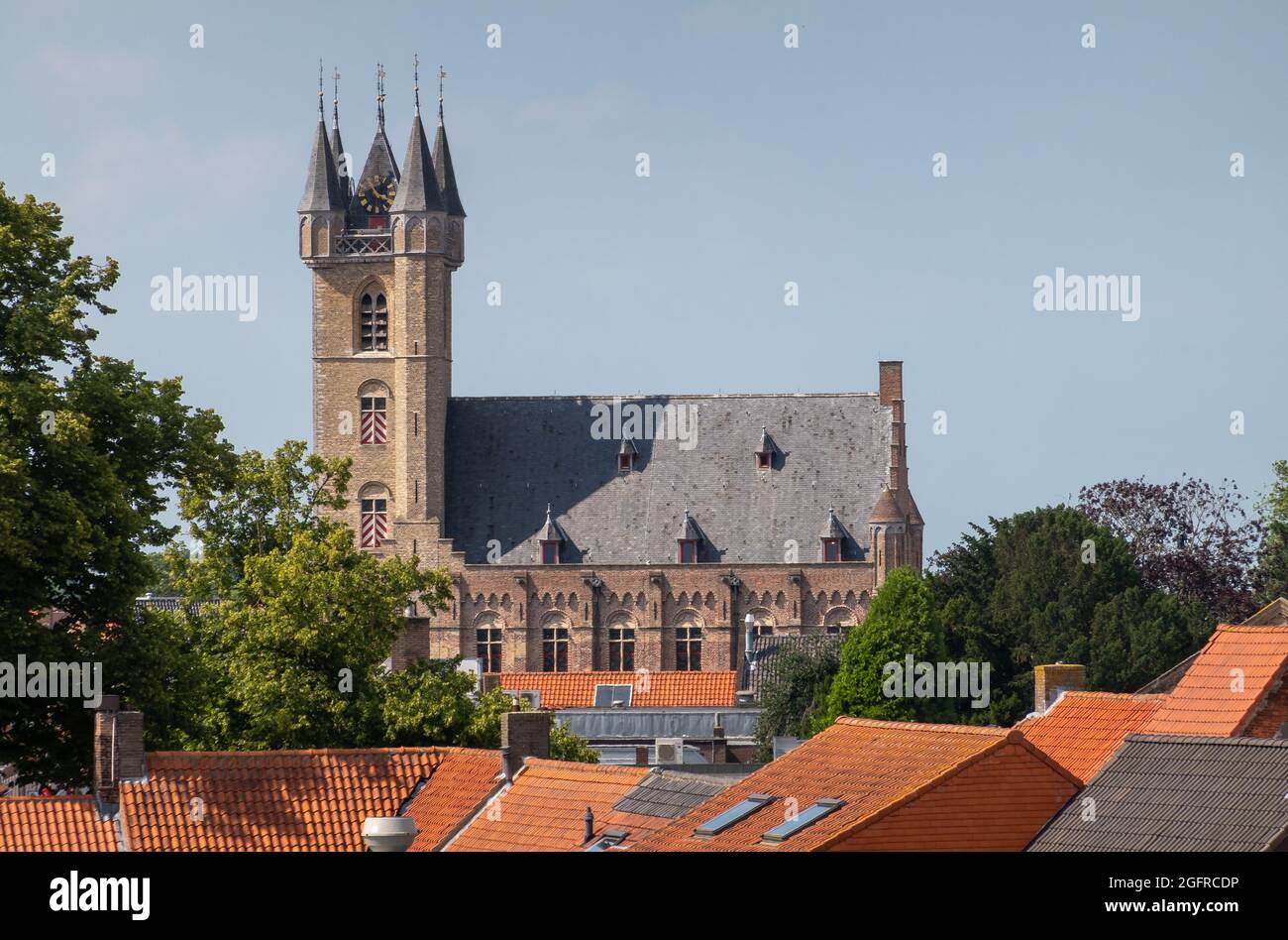 Sluis, Paesi Bassi - 5 agosto 2021: Il campanile che torreggia sopra le case cittadine con tetti rossi sotto il paesaggio blu nuvoloso. Qualche fogliame verde. Foto Stock