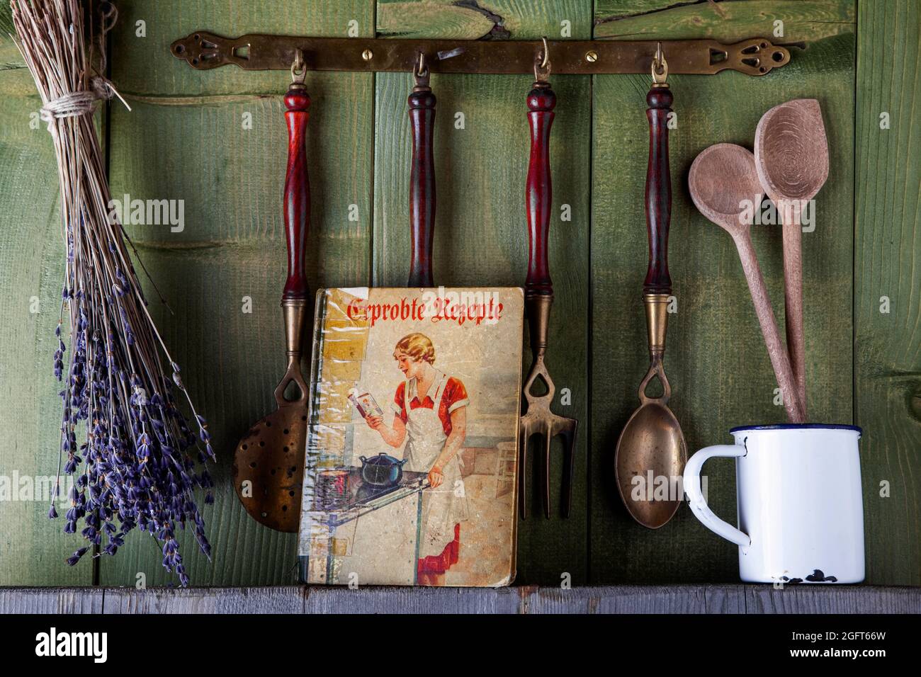 vecchio libro di cucina con utensili da cucina di fronte al muro di legno verde Foto Stock