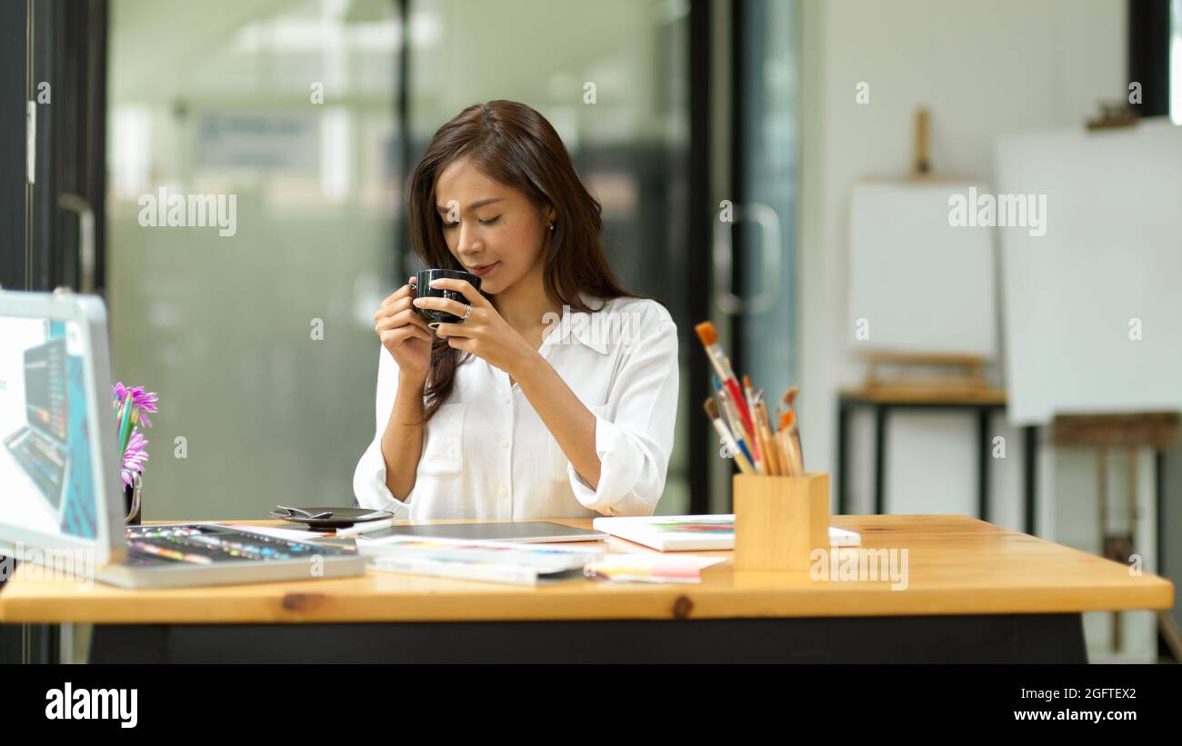 Designer grafico soddisfatto che prende pausa dal lavoro bevendo caffè, tempi di relax dopo il lavoro-duro in studio Foto Stock