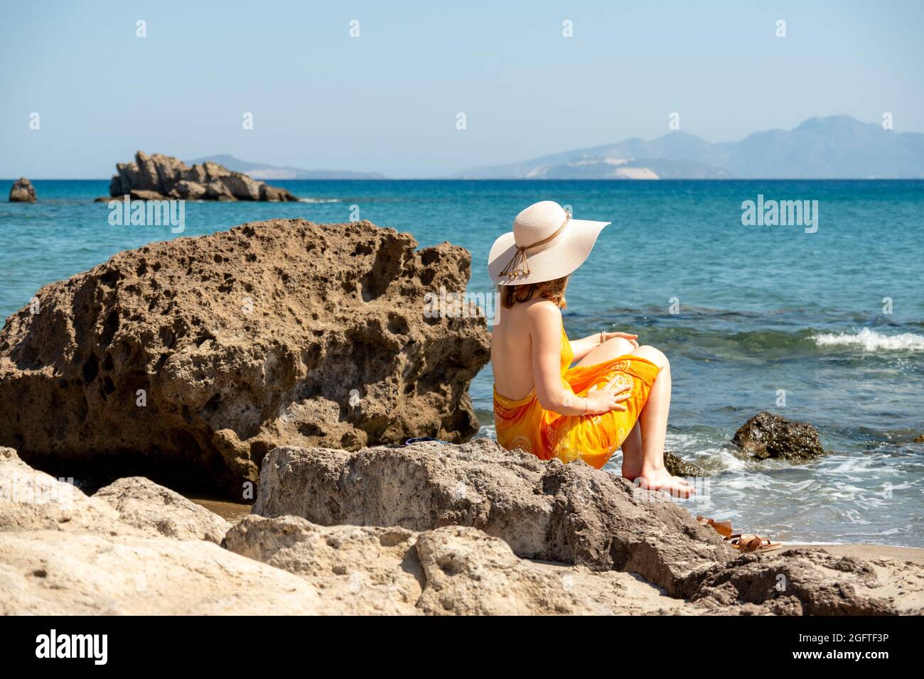 Donna sulla spiaggia di sabbia guardando le acque turchesi di fronte a Kos Foto Stock
