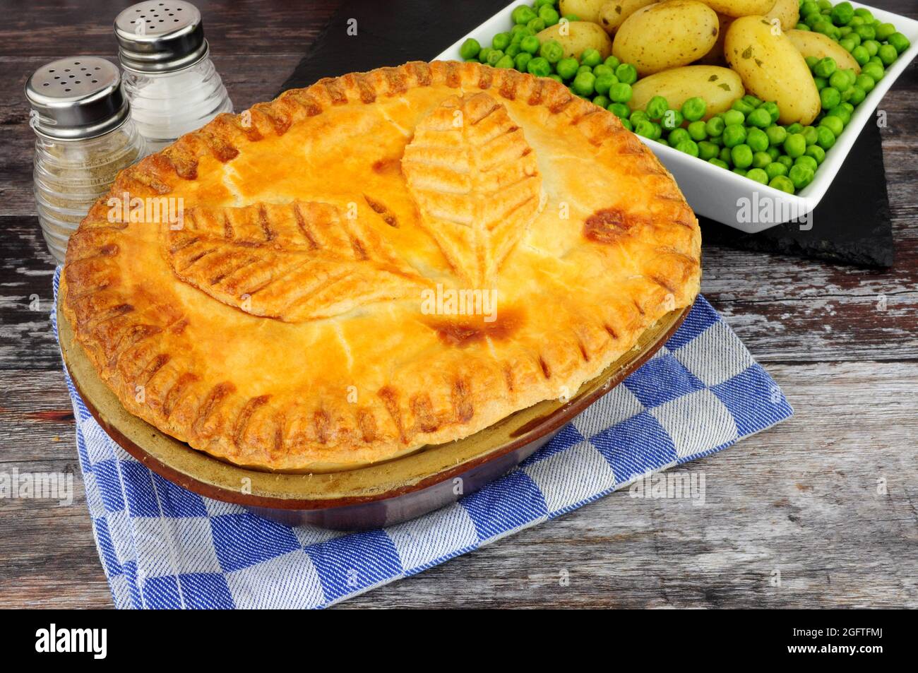 Torta di bistecca di manzo in una scatola di pasta frolla glassata con decorazione a foglia di pasta servita con patate novelle e contorno di piselli da giardino Foto Stock