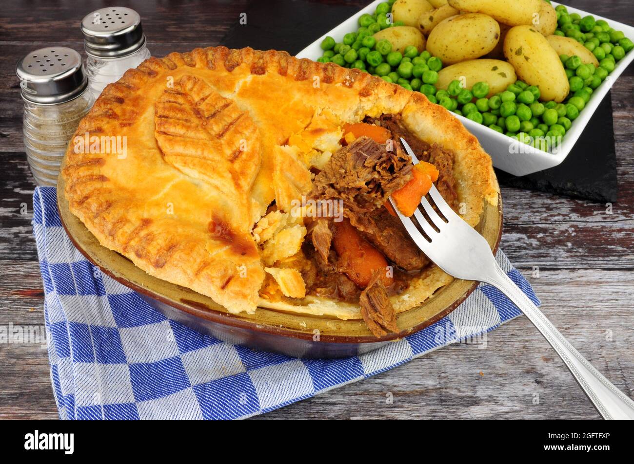 Torta di bistecca di manzo in una scatola di pasta frolla glassata con decorazione a foglia di pasta servita con patate novelle e contorno di piselli da giardino Foto Stock