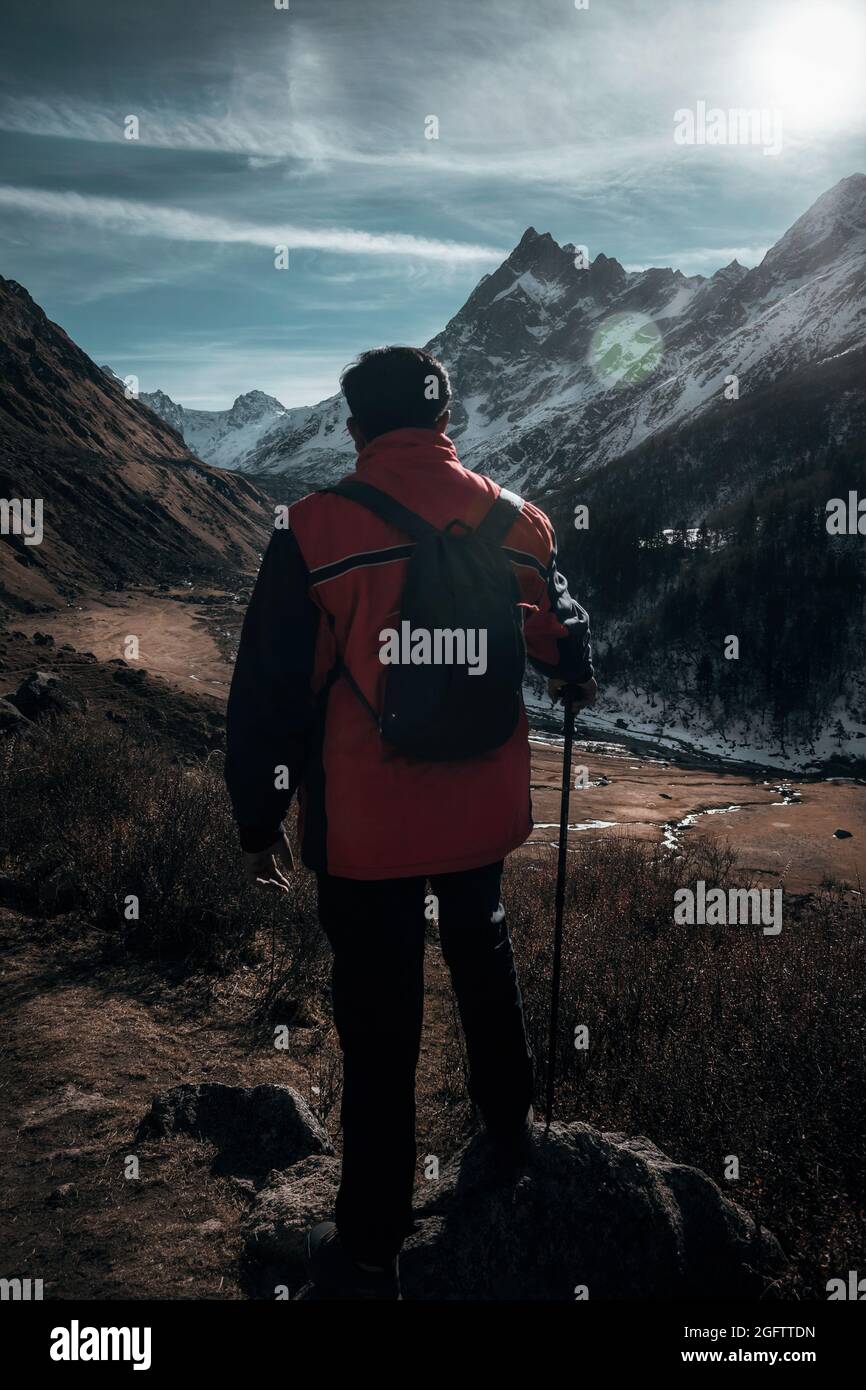 Ritratto di viaggio di uno zaino con volto nascosto con il suo palo da trekking guardando verso le montagne e la valle di fronte a lui Foto Stock