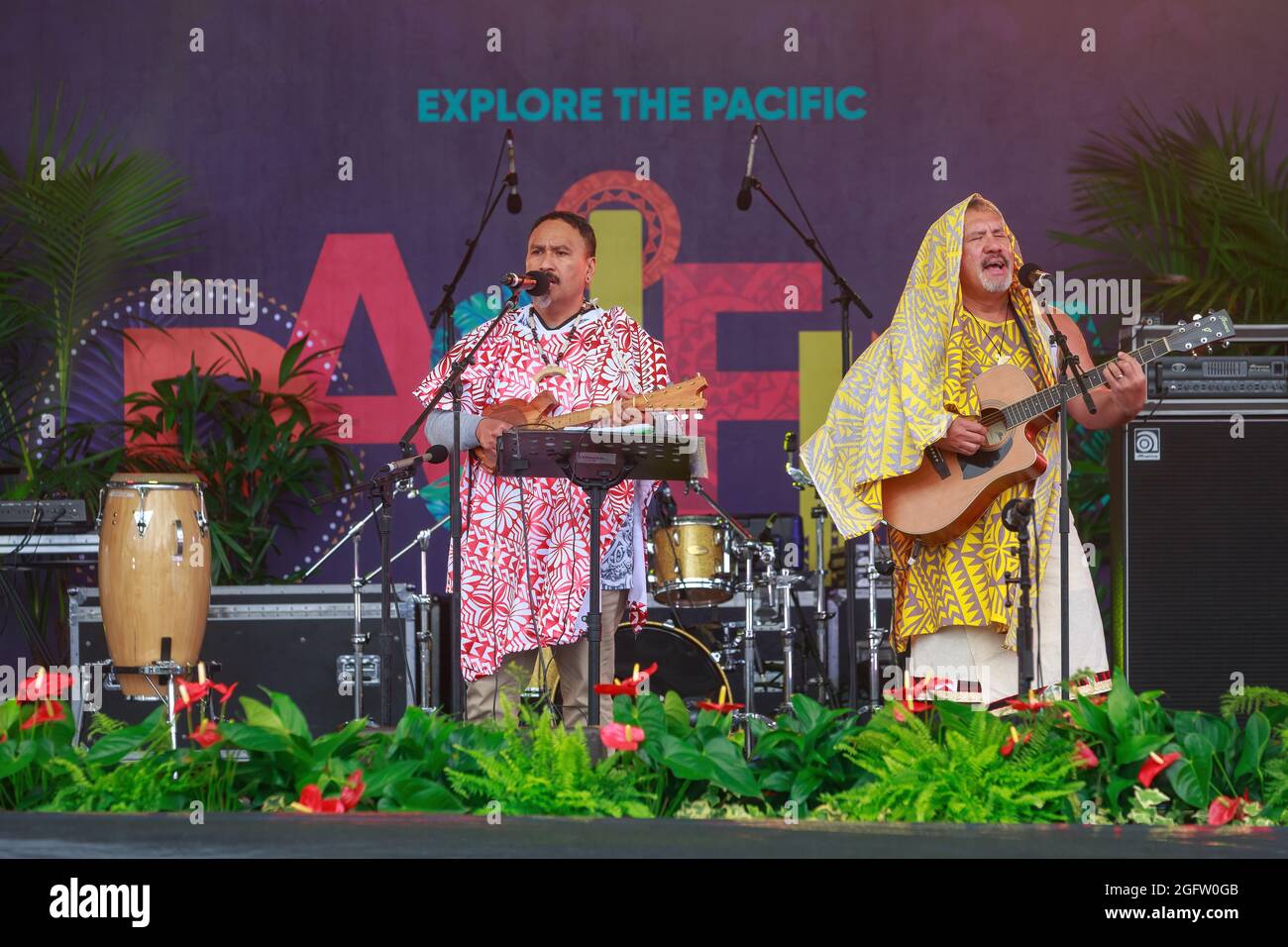 Due uomini hawaiani in costumi colorati cantano e suonano strumenti musicali al Festival Pasifika della cultura dell'Isola del Pacifico, Auckland, Nuova Zelanda Foto Stock