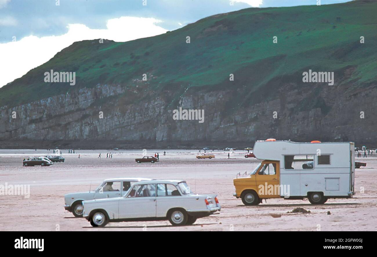 Storico 1977 archivio vista degli anni '70 Ford Transit basato scopo costruito Camper furgone tra le auto parcheggiate sul Ministero aziendale Di Defense Pendine sabbia sotto Gilman Point con persone che godono il sole e la bassa marea in Archival vista del Siamo stati negli anni '70 lungo il paesaggio costiero di Carmarthen Bay sulla costa del Carmarthenshire del Sud Litorale del Galles Regno Unito Foto Stock