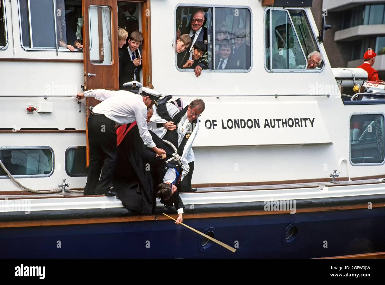 Primo piano storico degli anni '90 vista archivio della vecchia usanza & tradizione di battere i limiti effettuata nel 1992 Dalla chiesa di tutti gli Hallows presso la torre con l'aiuto del clero della chiesa e ragazzi della scuola del St Dunstan's College & personale assistito da equipaggio PLA nel tenere un ragazzo capovolto in corda da un porto di Londra degli anni '90 Lancio autorità per battere il confine sud in acqua di fiume con una canna un evento insolito nel mezzo di River Thames un'immagine d'archivio nella City of London England UK Foto Stock