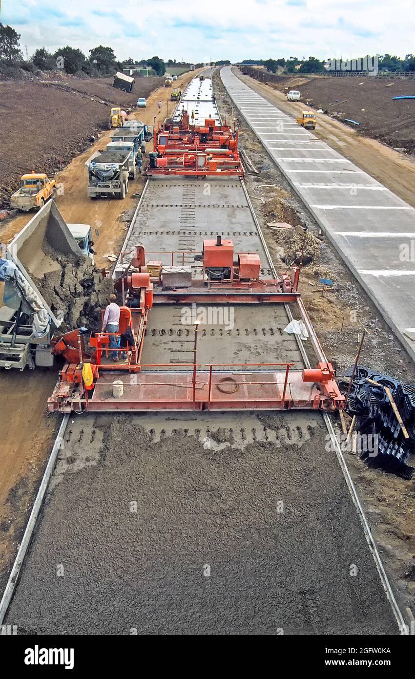 Archival 1986 veduta aerea dei lavoratori appaltatori che ricevono consegne di calcestruzzo da autocarri con ribaltamento laterale a macchine per la posa su strada in Ingegneria civile infrastrutture di trasporto costruzione cantiere una nuova A12 trunk Road bypass strada a doppia carreggiata strada che bypassa la città Di Chelmsford con membrana di politene in posizione in Essex Inghilterra UK un archivio storico 1980 immagine prima di cappelli duri e. giacche ad alta visibilità Foto Stock