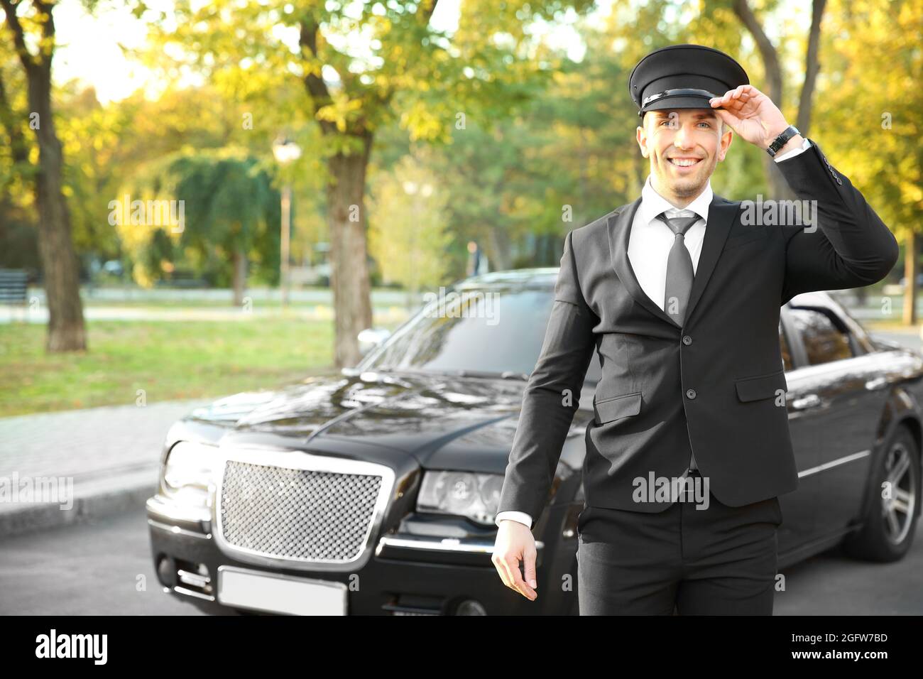 Giovane autista che regola cappello vicino auto di lusso sulla strada Foto  stock - Alamy