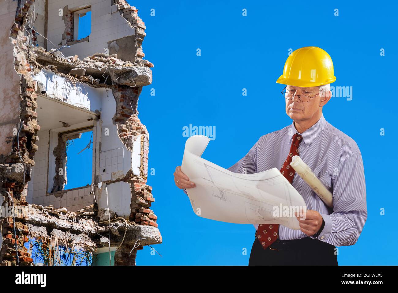 architetto con progetto di costruzione e elmetto, demolizione edificio in background Foto Stock