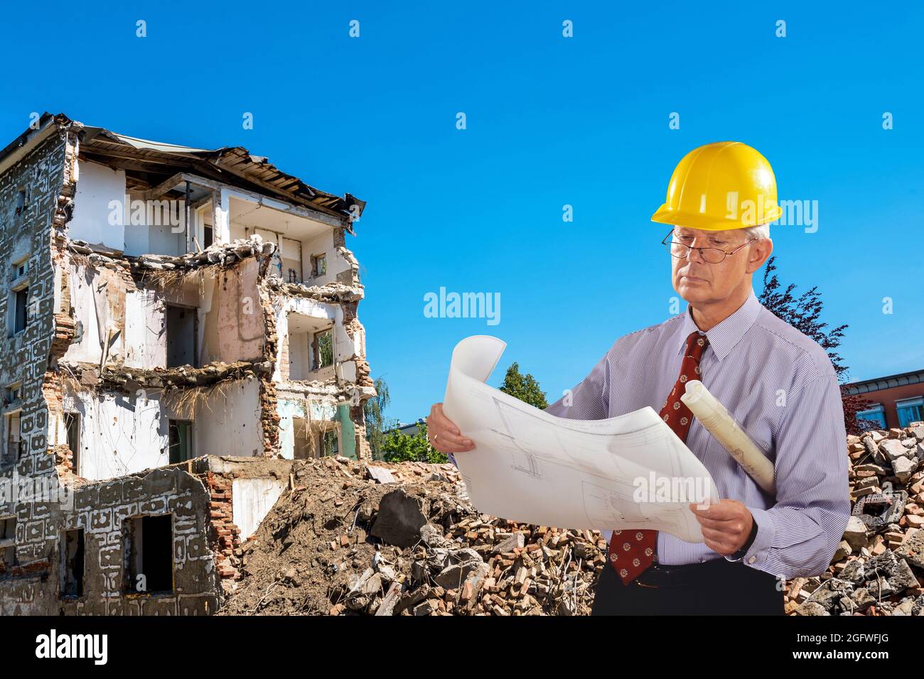 architetto con progetto di costruzione e elmetto, demolizione edificio in background Foto Stock