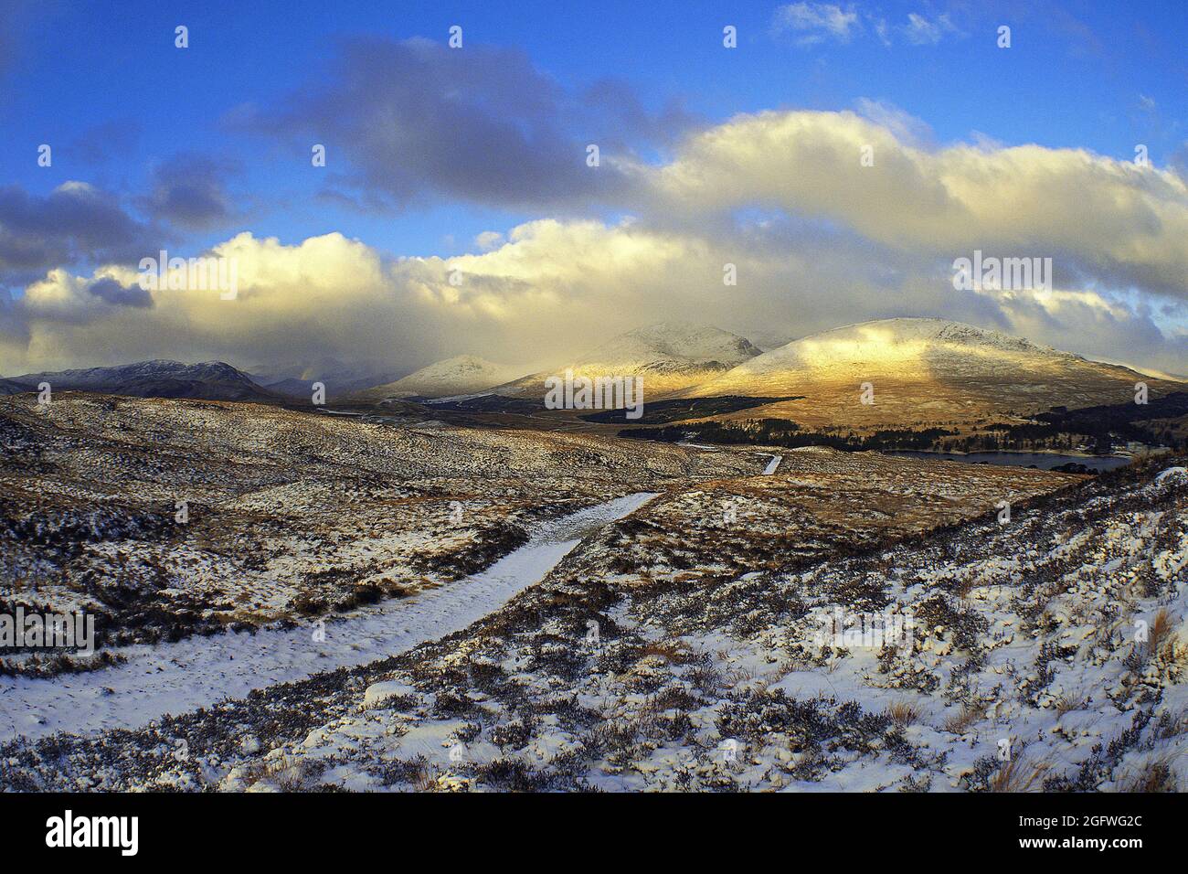 La pista di montagna conduce attraverso la brughiera parzialmente innevata verso le colline nuvolose di Blackmount, Rannoch Moor, Regno Unito, Scozia, Highland Foto Stock