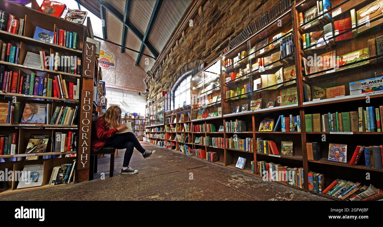 Barter Books, Alnwick Station, Northumberland. Giovane donna che prende un rapido Peek Foto Stock