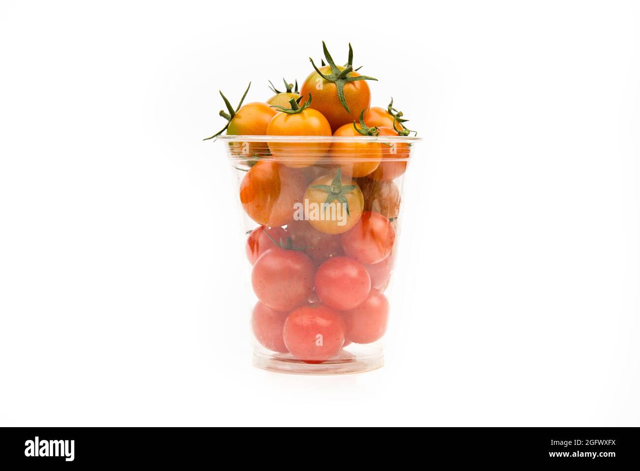 Pomodori ciliegini in contenitore trasparente di plastica su sfondo bianco, primo piano. Foto Stock