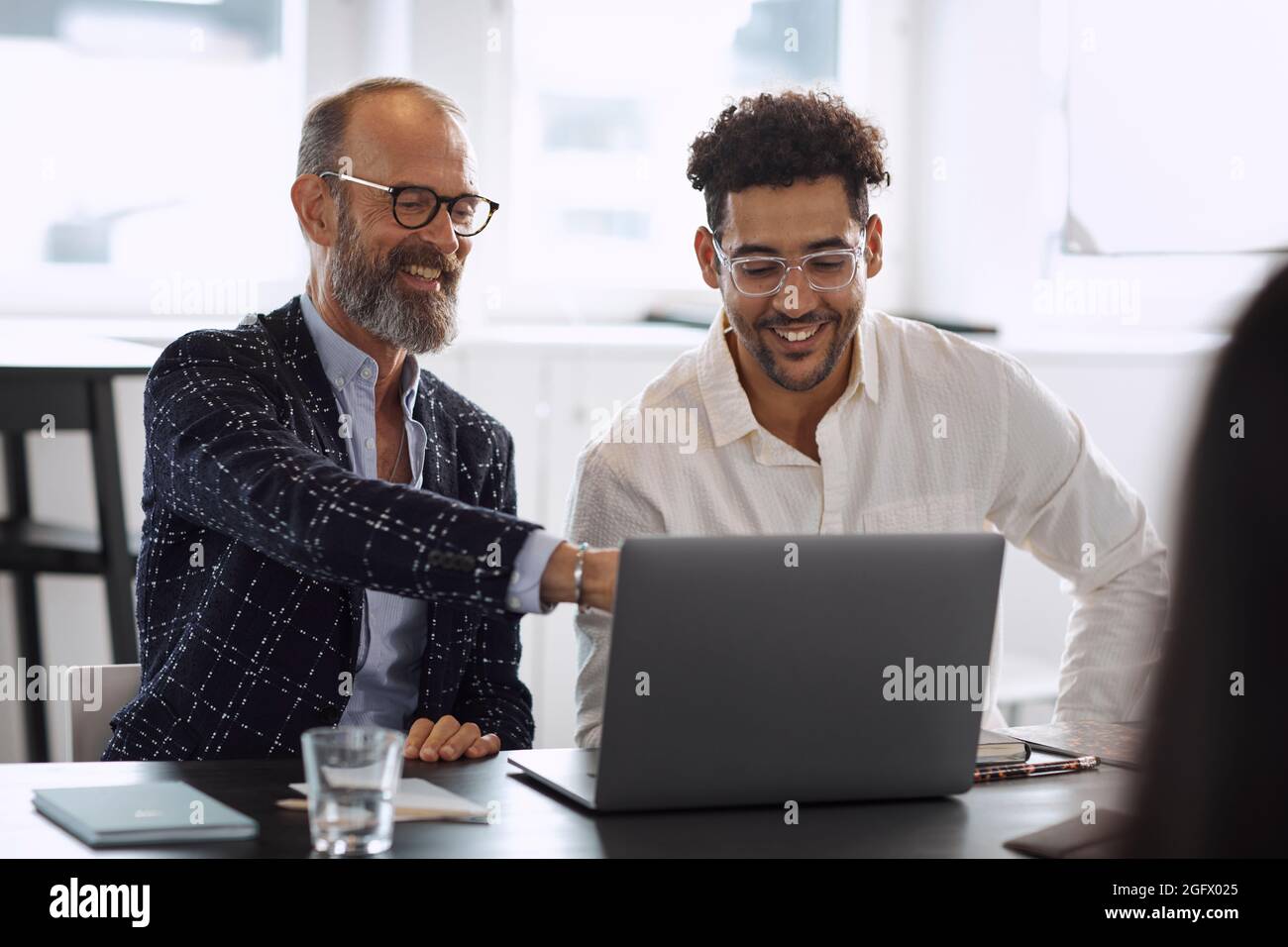 Uomini che usano un computer portatile durante una riunione d'affari Foto Stock