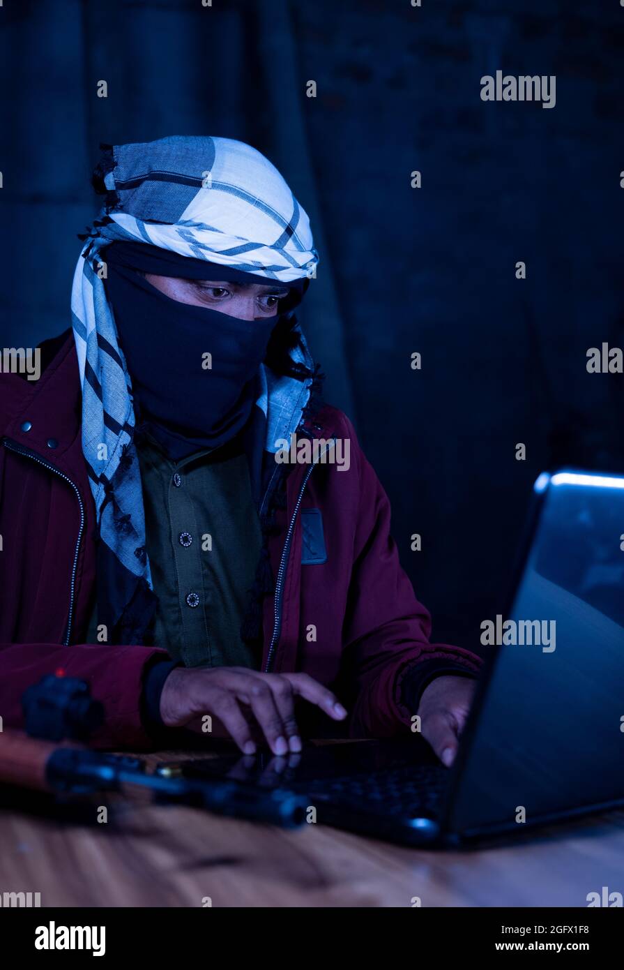 Militante islamico con visone di copertura e pistola sul tavolo con laptop per hack - concetto di moderno cyber terrorismo o cyber attacchi Foto Stock