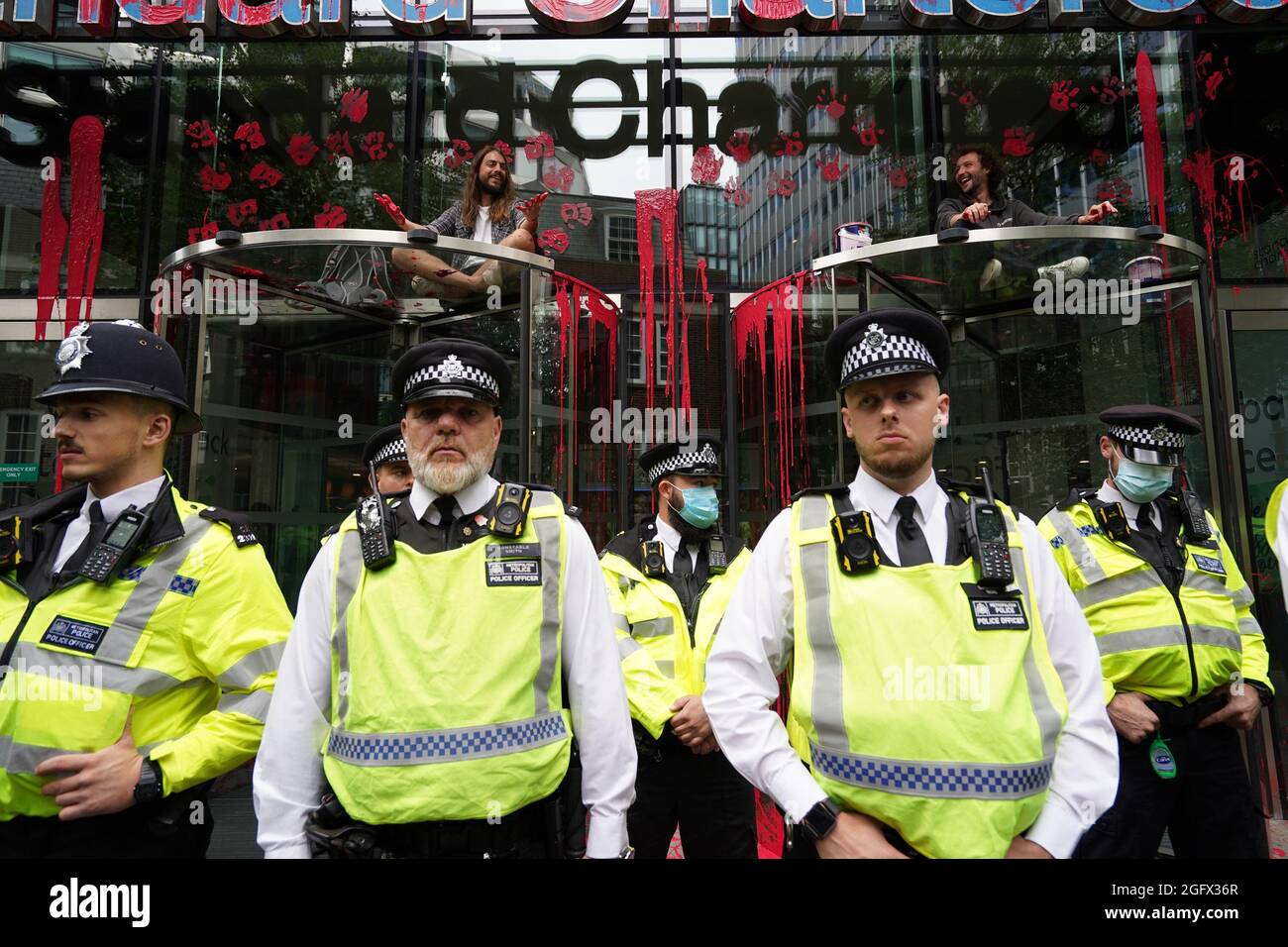 I dimostranti si siedono sopra le porte dell'edificio Standard Chartered, che è stato scolorito, mentre gli ufficiali di polizia bloccano l'accesso mentre una protesta della ribellione dell'estinzione attraversa la città di Londra. Data foto: Venerdì 27 agosto 2021. Foto Stock