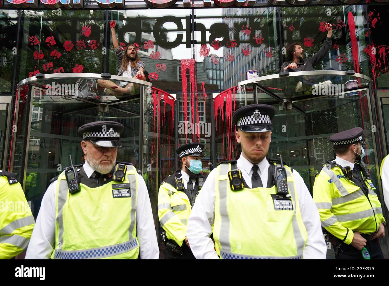I dimostranti si siedono sopra le porte dell'edificio Standard Chartered, che è stato scolorito, mentre gli ufficiali di polizia bloccano l'accesso mentre una protesta della ribellione dell'estinzione attraversa la città di Londra. Data foto: Venerdì 27 agosto 2021. Foto Stock