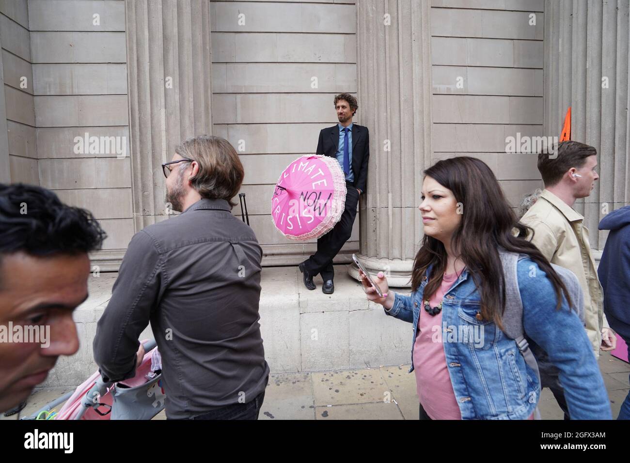 La gente cammina davanti a un dimostratore durante una protesta da parte dei membri della ribellione di estinzione alla Banca d'Inghilterra, nella città di Londra. Data foto: Venerdì 27 agosto 2021. Foto Stock