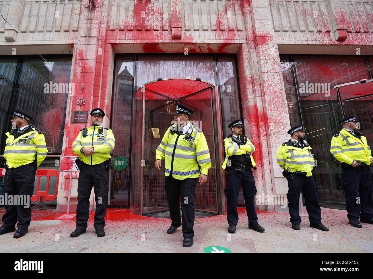 Gli ufficiali di polizia si trovano di fronte a uno degli edifici della Guildhall, che è stato scolorito, mentre una protesta della ribellione dell'estinzione si fa strada attraverso la città di Londra. Data foto: Venerdì 27 agosto 2021. Foto Stock