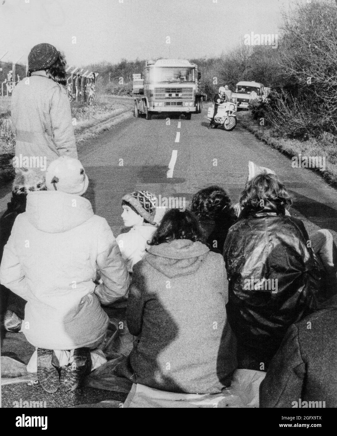 Le donne del Greenham Common Womens Peace Camp si siedono attraverso una strada che ostruisce il traffico, tra cui una motocicletta e un camion della polizia. Foto Stock