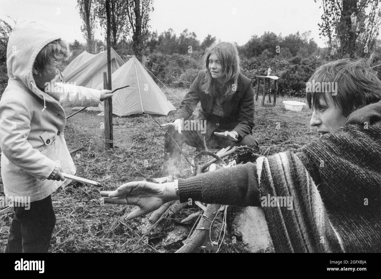 Ottobre 1981. Greenham Common Peace Camp. Due donne e un bambino attorno ad un fuoco aperto che interagisce con tende sullo sfondo. Foto Stock