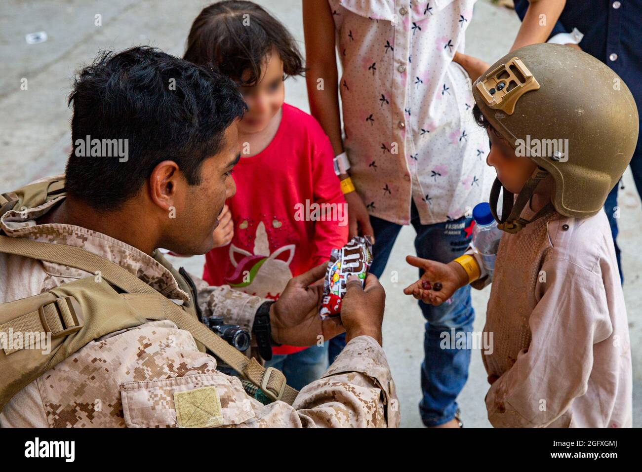 Una Marina statunitense con Special Purpose Marine Air-Ground Task Force - Crisis Response - Central Command, dà caramelle ai bambini durante un'evacuazione all'Aeroporto Internazionale Hamid Karzai, Kabul, Afghanistan, 24 agosto. I membri del servizio degli Stati Uniti stanno assistendo il Dipartimento di Stato con un'operazione DI evacuazione non combattente (NEO) in Afghanistan. (STATI UNITI Foto del corpo marino di Lance CPL. Nicholas Guevara) Foto Stock