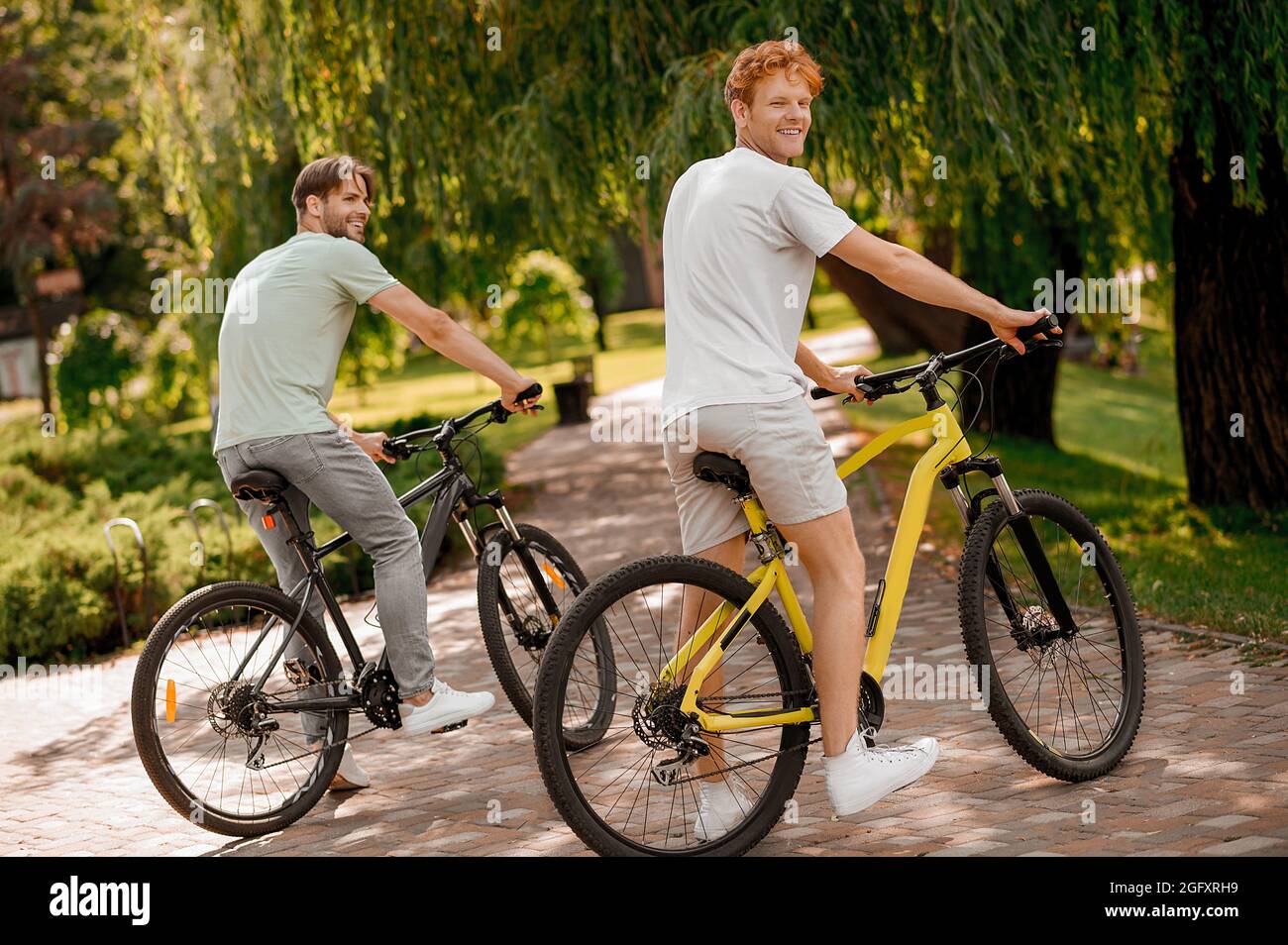 Due bei uomini di vestibilità che cavalcano le loro biciclette in un parco Foto Stock