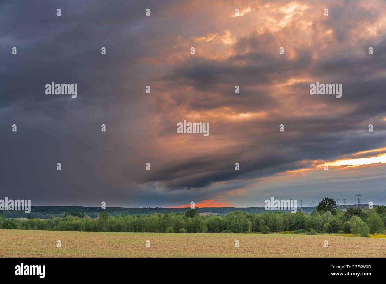 Una strada sterrata attraverso una vasta pianura. Il cielo è leggermente nuvoloso. La sera sta arrivando e il sole tramontato con la sua luce trasforma le nuvole in un colore rosso. Foto Stock