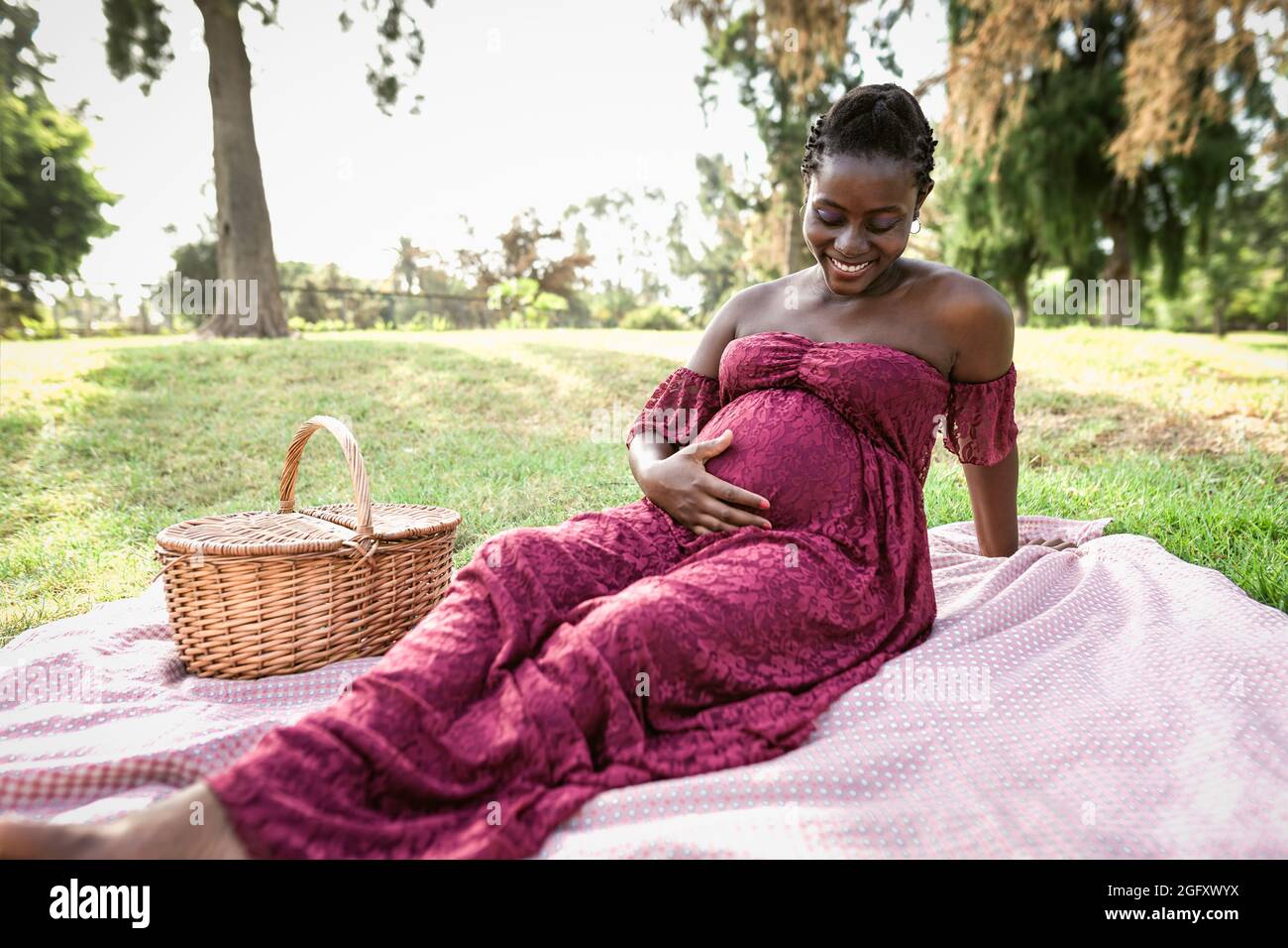 Donna africana carezzando il suo ventre incinta mentre fa un picnic nel parco - concetto di stile di vita di maternità Foto Stock
