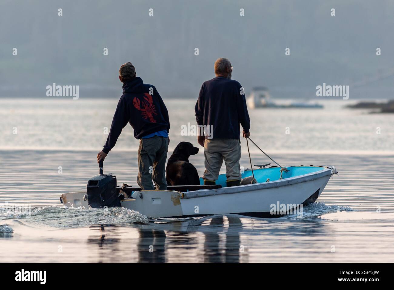 Due uomini e un cane che si dirigono verso l'esterno sullo skiff per lavorare sulla barca di aragosta Maine Foto Stock