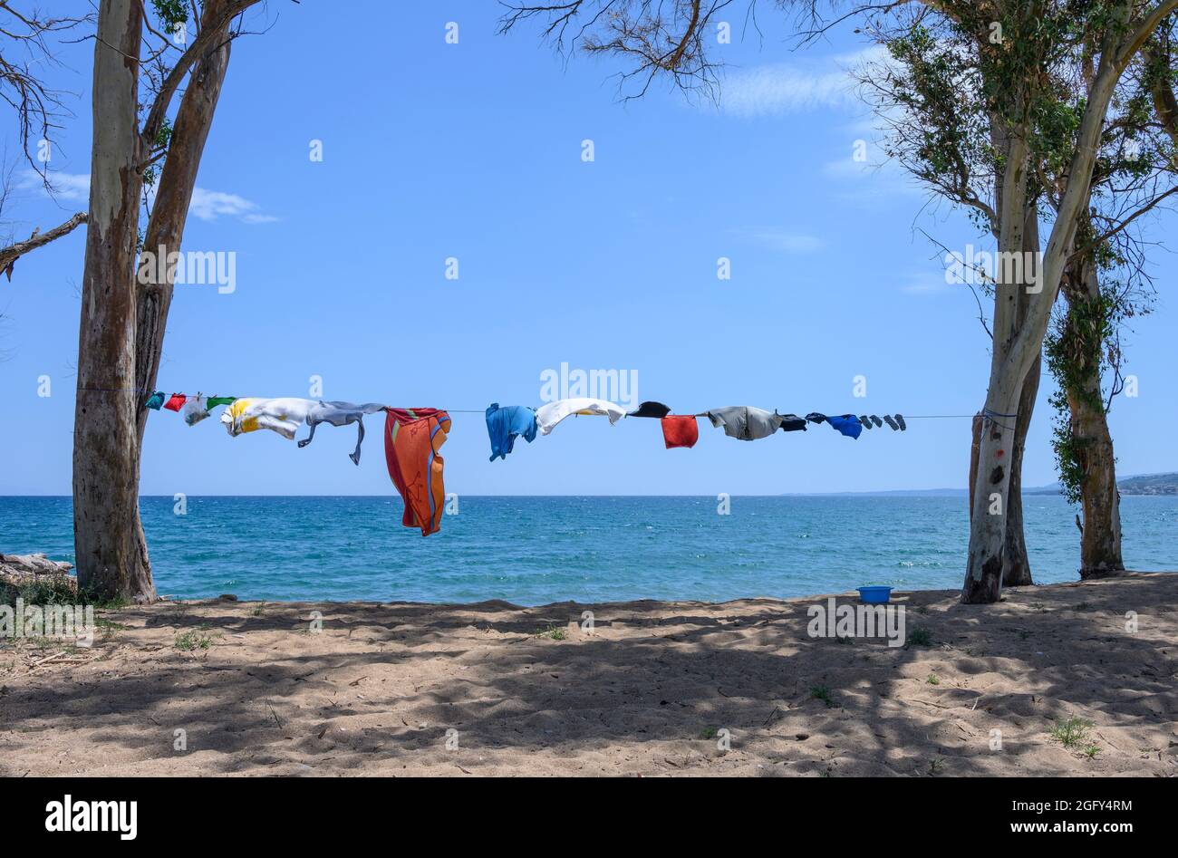 Camper vestiti che asciugano su una linea di lavaggio, tra alberi, vicino al mare su una spiaggia nel sud della Grecia. Foto Stock