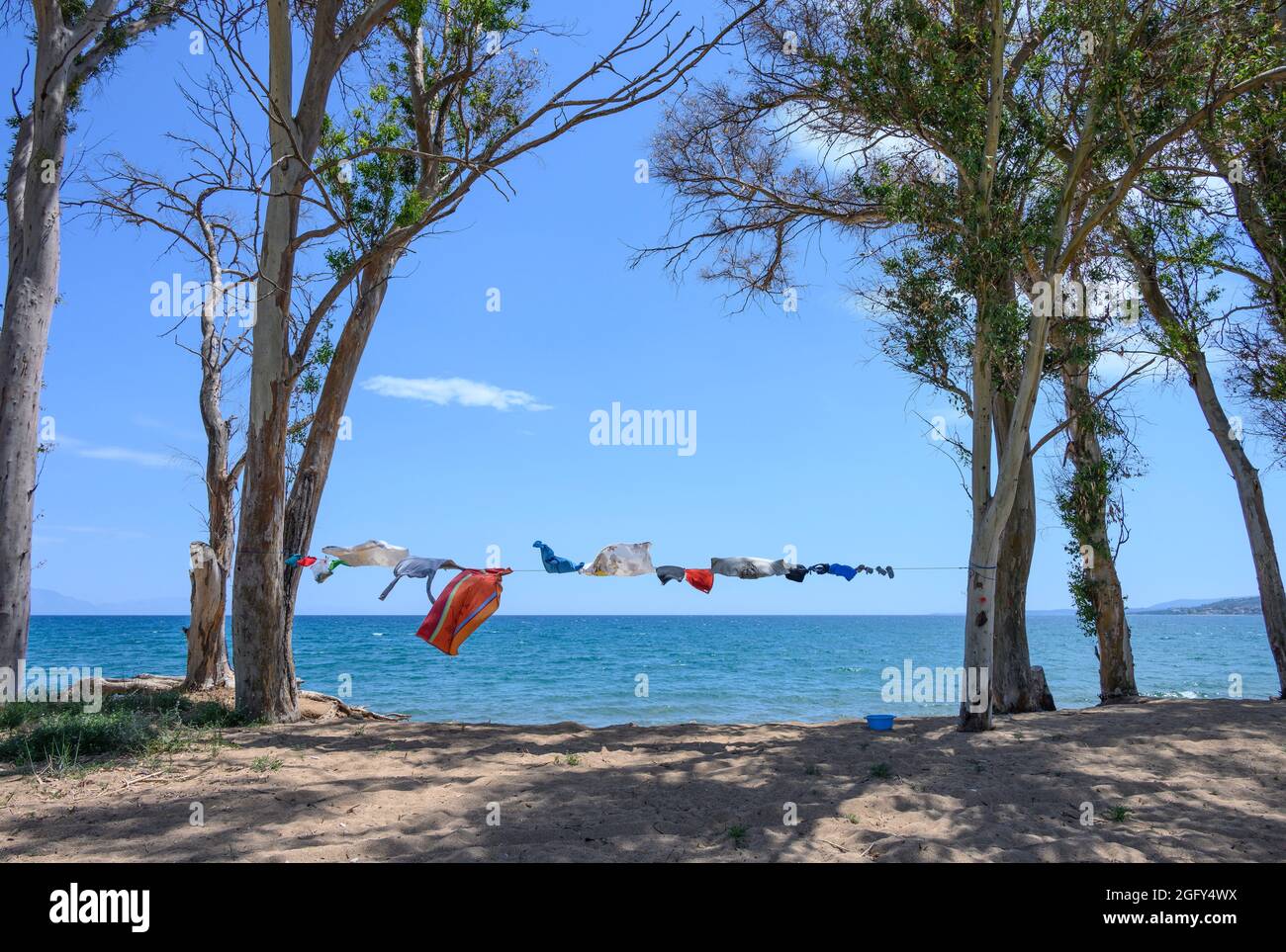 Camper vestiti che asciugano su una linea di lavaggio, tra alberi, vicino al mare su una spiaggia nel sud della Grecia. Foto Stock