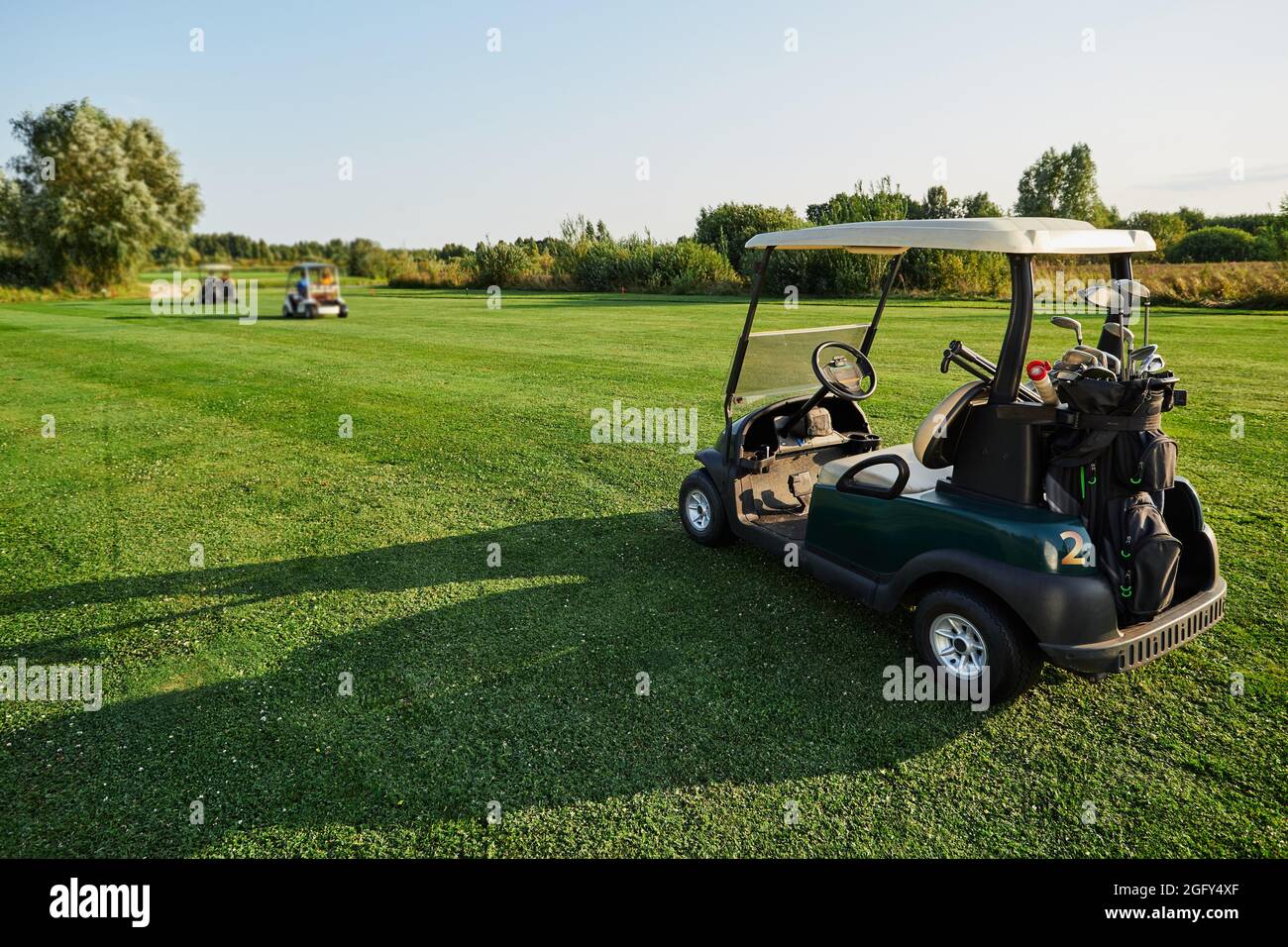 Golf car con club e attrezzature si trova sul campo da golf in erba con una lunga ombra durante il golf Foto Stock