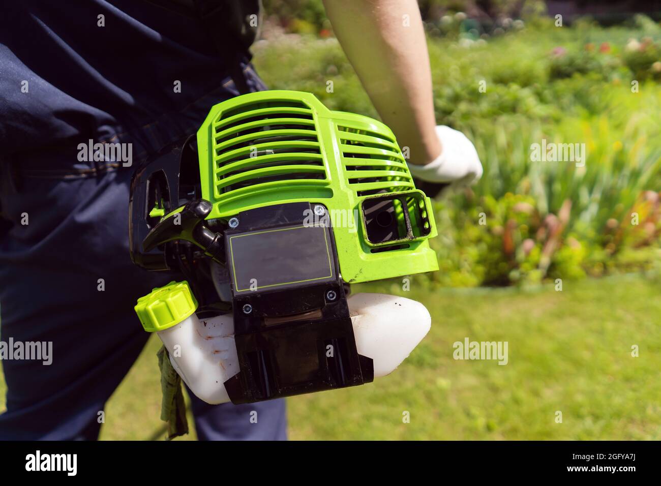 Un primo piano di un giovane bianco che muove un prato con un rasaerba nelle mani Foto Stock