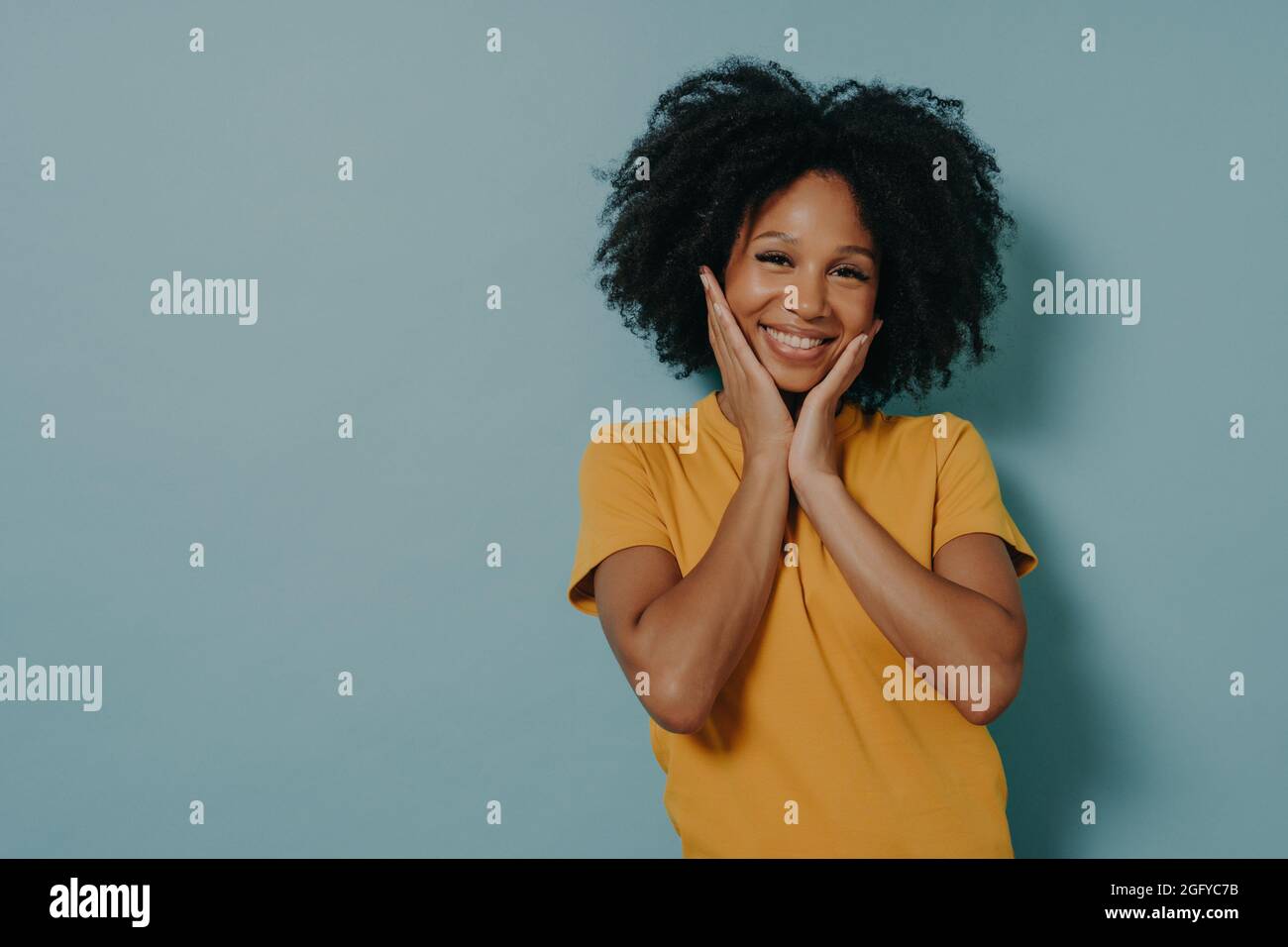 Cute gara mista giovane donna che tocca le guance con le mani e si sente felice dopo aver sentito il complimento Foto Stock