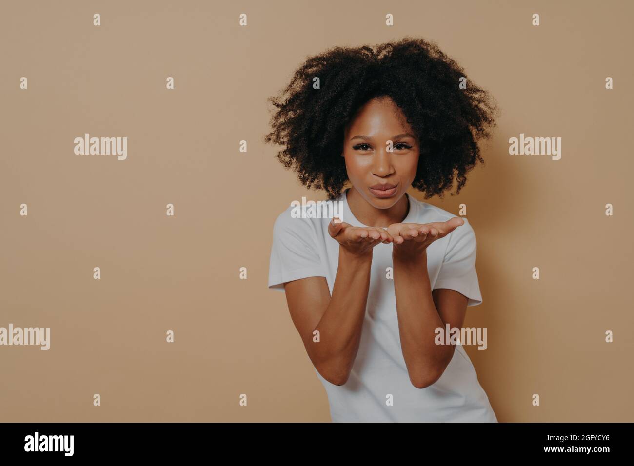 Bella ragazza africana curly flirty invio aria bacio e sorridente mentre si posa su sfondo beige Foto Stock