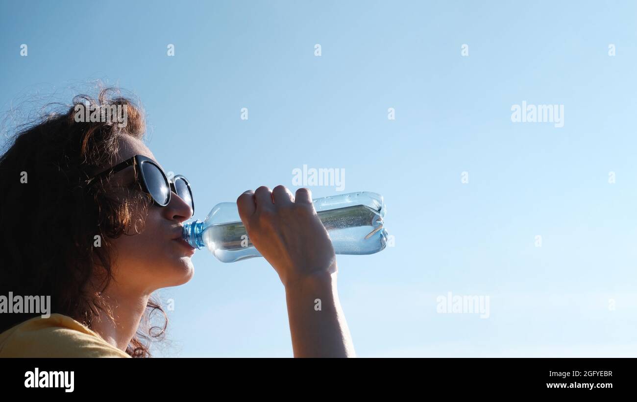 Ragazza con bicchieri beve acqua da una bottiglia in tempo caldo. Foto Stock