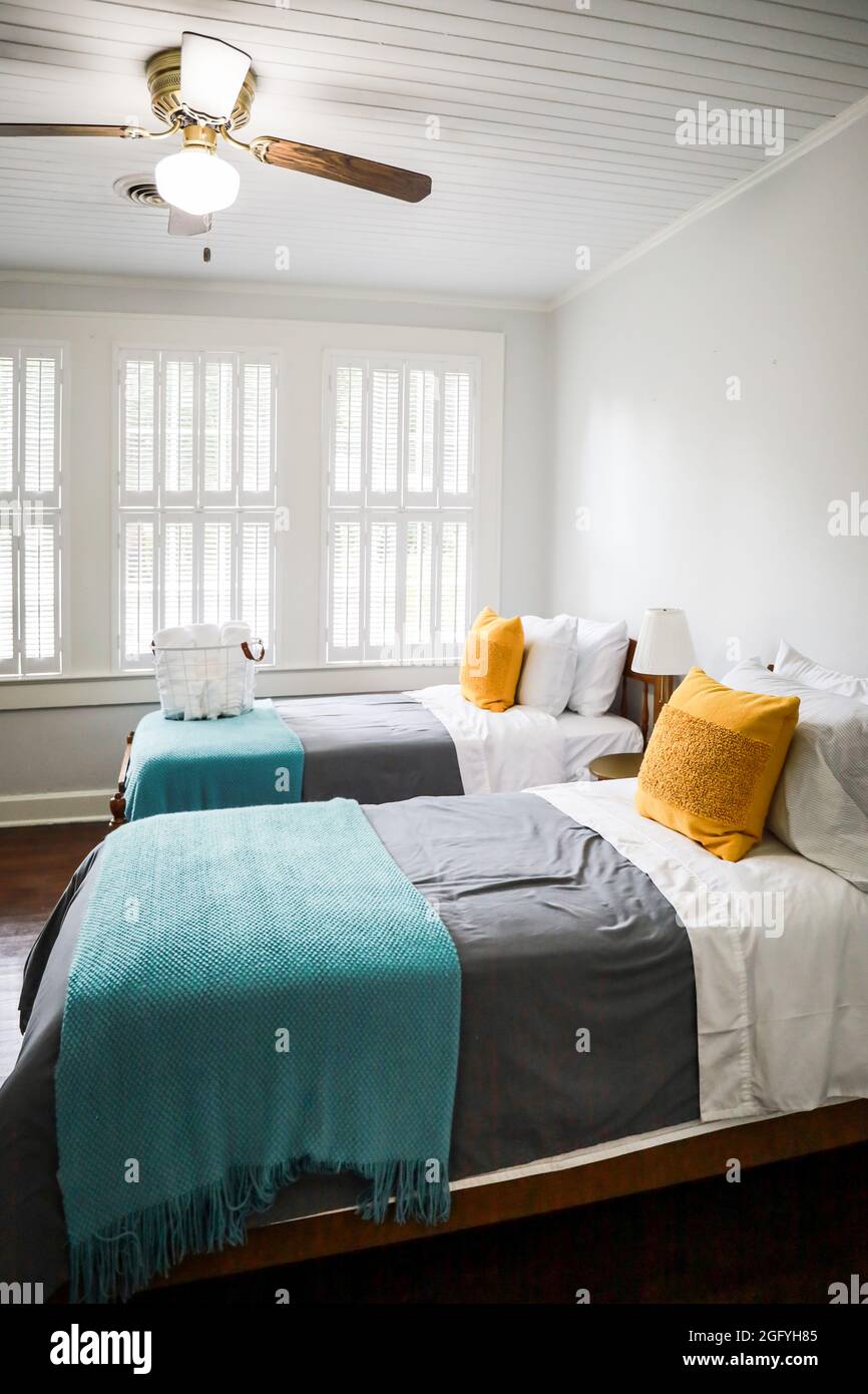 Una camera da letto con due letti singoli con copriletto color turchese e grigio e cuscini decorativi gialli Foto Stock